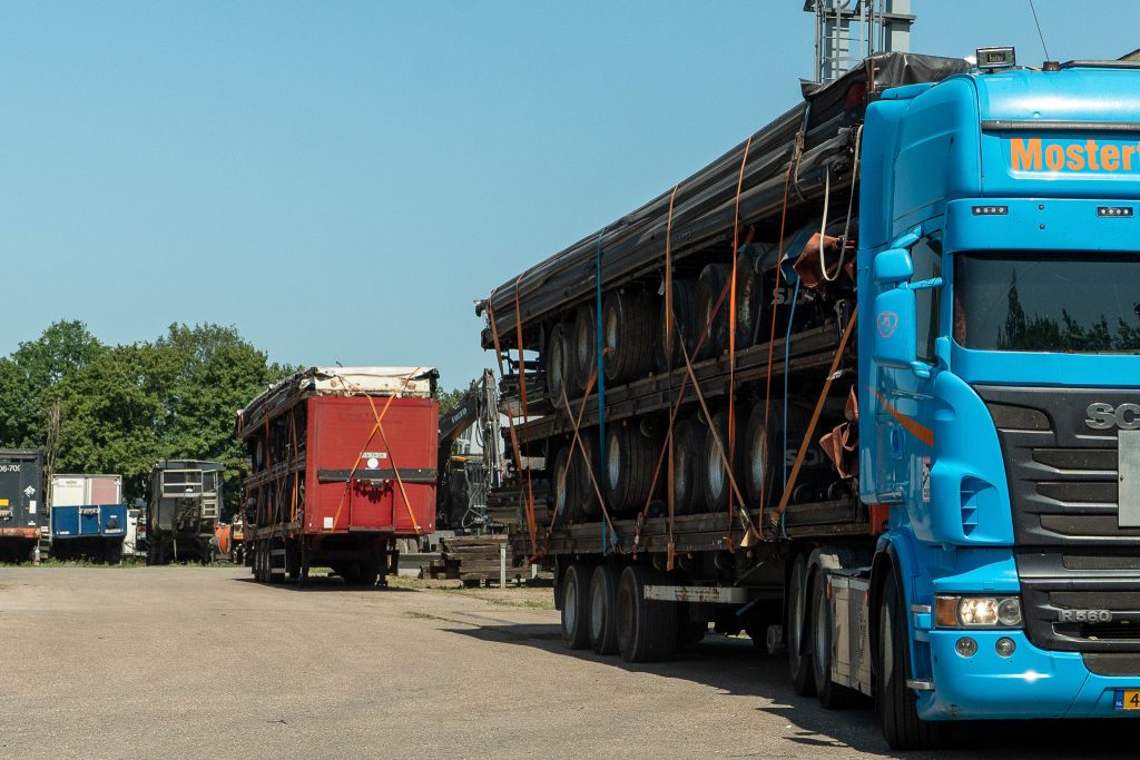 Mostert Scrap terrein met vrachtwagen en schrootcontainers op een zonnige dag.